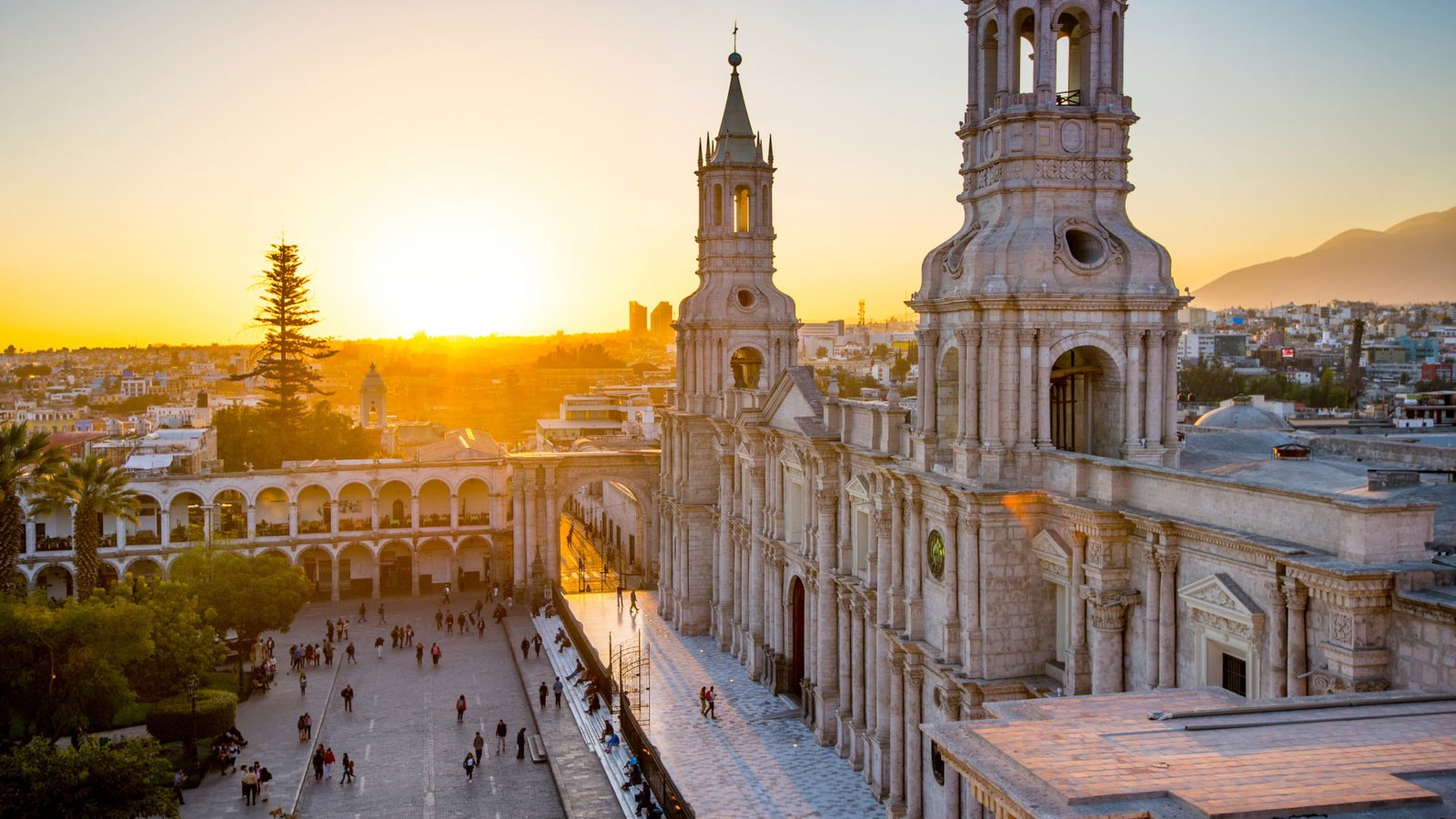 Fachada iluminada de la Catedral de Arequipa durante el atardecer con personas en la plaza.