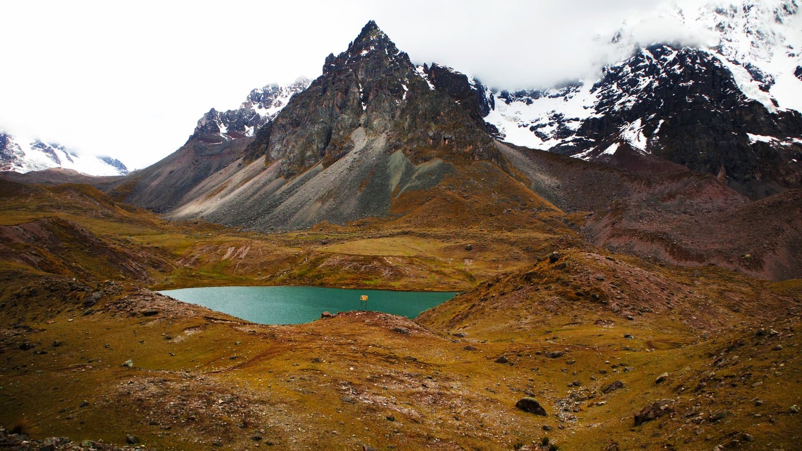 Montaña escarpada frente a una laguna color esmeralda en los Andes.