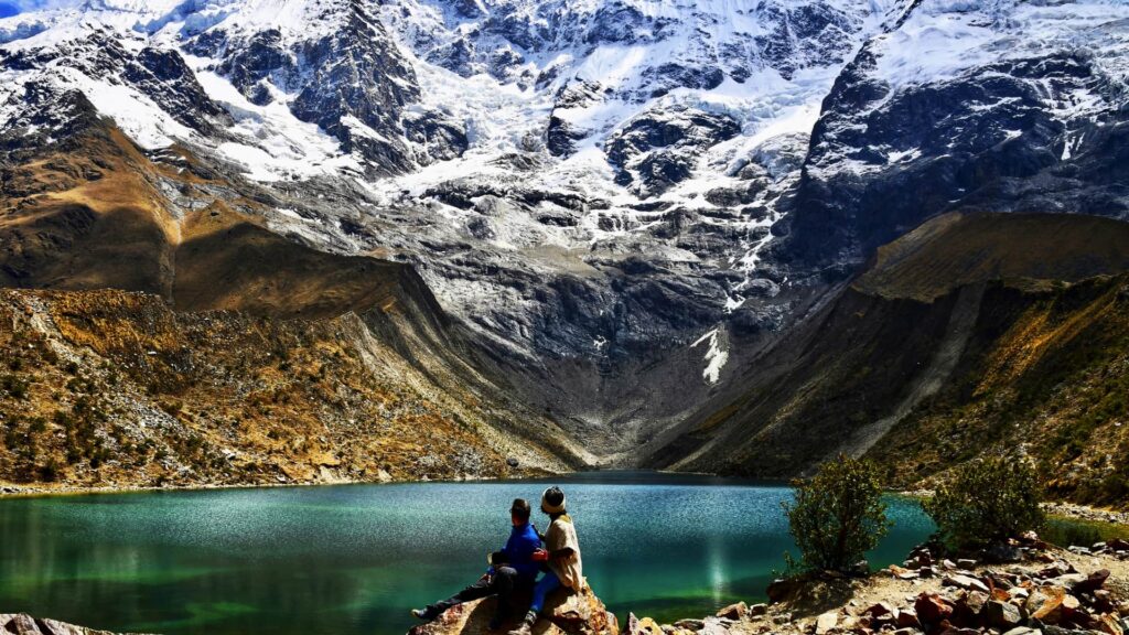 Dos personas sentadas frente a la Laguna Humantay contemplando el paisaje glaciar.