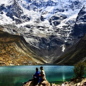 Dos personas sentadas frente a la Laguna Humantay contemplando el paisaje glaciar.