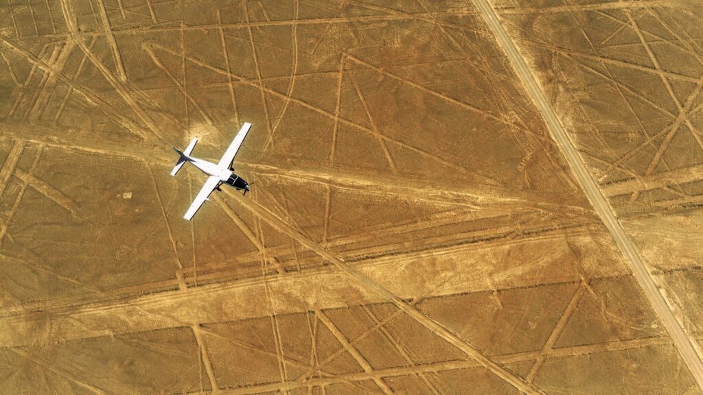 Avioneta blanca volando sobre los geoglifos y trazos lineales del desierto de Nazca.