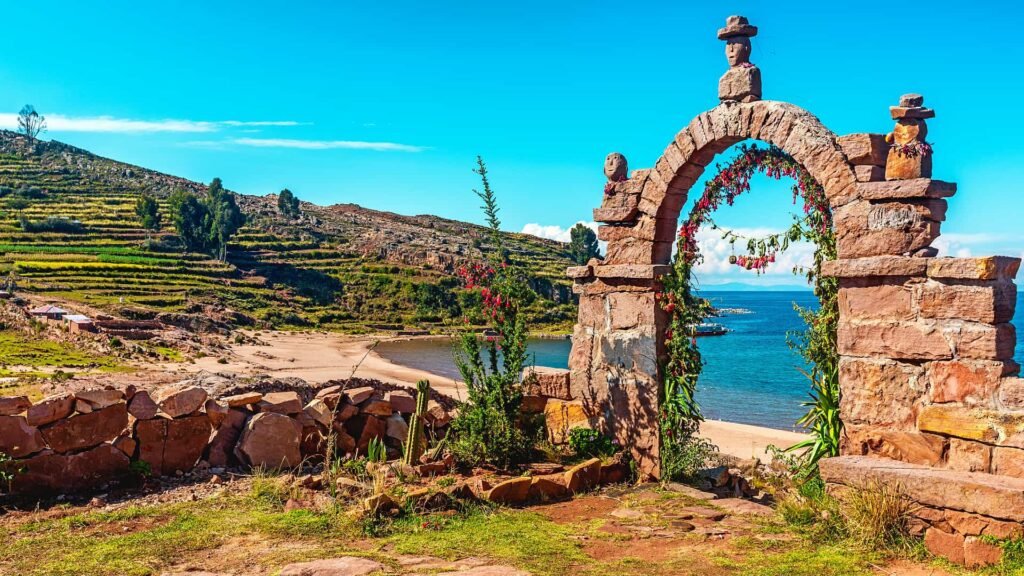 Un arco de piedra tradicional con vista a una playa de arena y el Lago Titicaca.