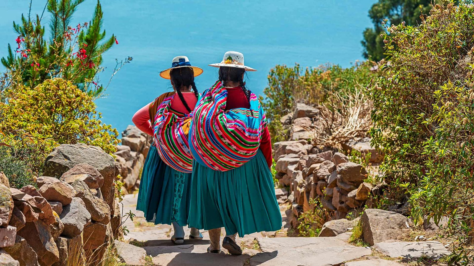 Dos mujeres caminando con mantas coloridas (llicllas) y polleras turquesas.