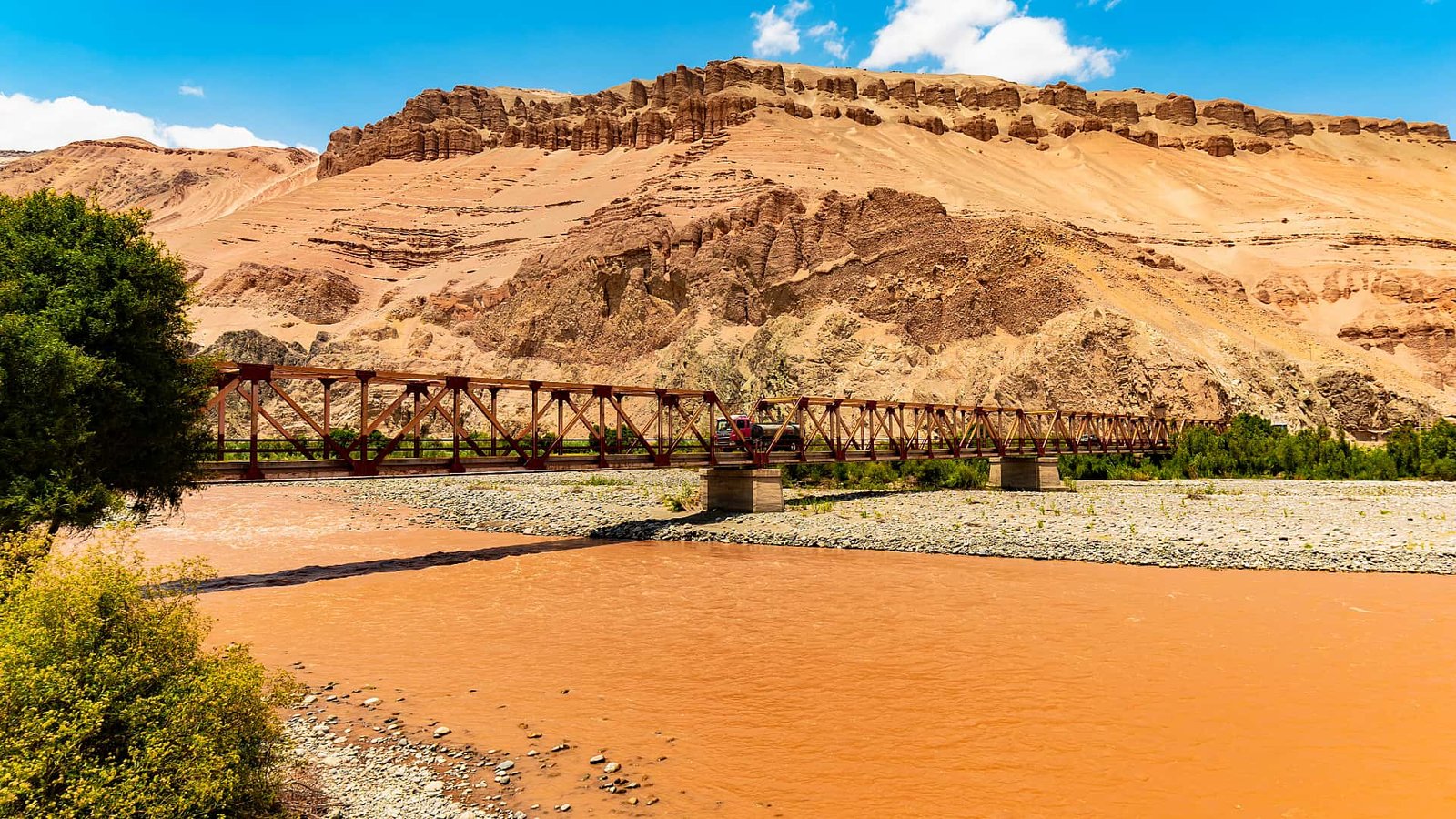 Vista panorámica del Valle de Majes con sus formaciones de tierra rojiza y un puente sobre el río.