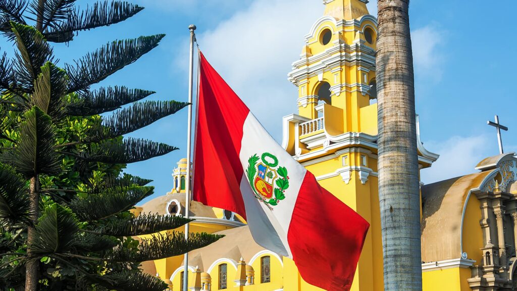 Bandera de Perú ondeando frente a edificios amarillos coloniales en Lima.