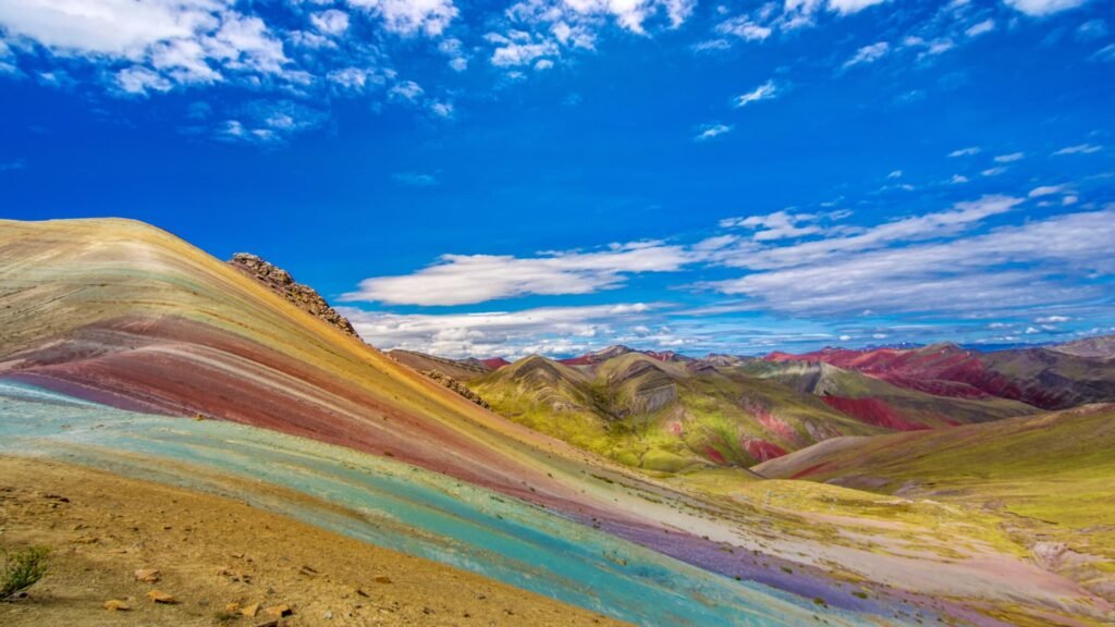 Paisaje vibrante de la Montaña de Colores bajo un cielo azul intenso con nubes blancas.