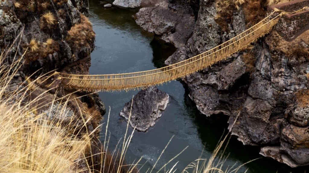 Puente de cuerdas incaico visto desde el lecho del río, mostrando la altura y los muros de piedra del cañón.