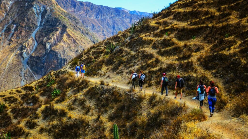 Grupo de excursionistas caminando en fila por un sendero estrecho y seco en la ladera de una montaña.