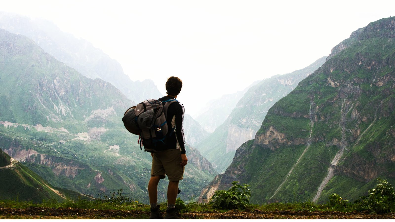 Hombre con mochila de montaña parado de espaldas contemplando la profundidad del cañón entre la neblina.