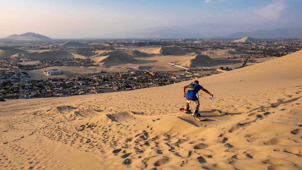 Turista practicando sandboarding bajando una duna de arena en Ica.