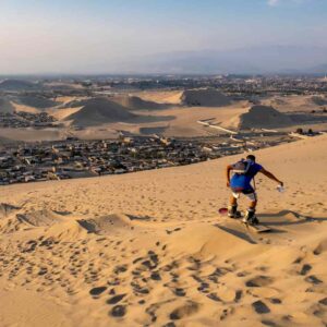 Turista practicando sandboarding bajando una duna de arena en Ica.