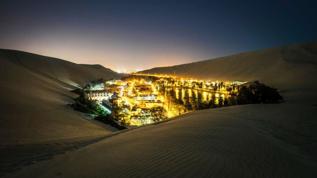 Luces nocturnas del pueblo de Huacachina rodeado por el desierto oscuro.