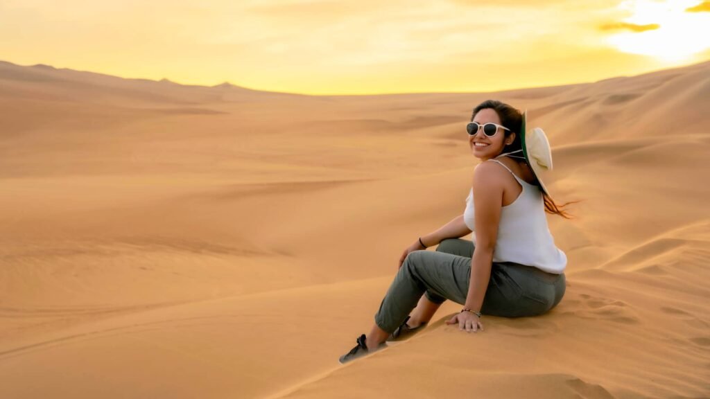 Mujer sentada en la arena contemplando el desierto de Ica.
