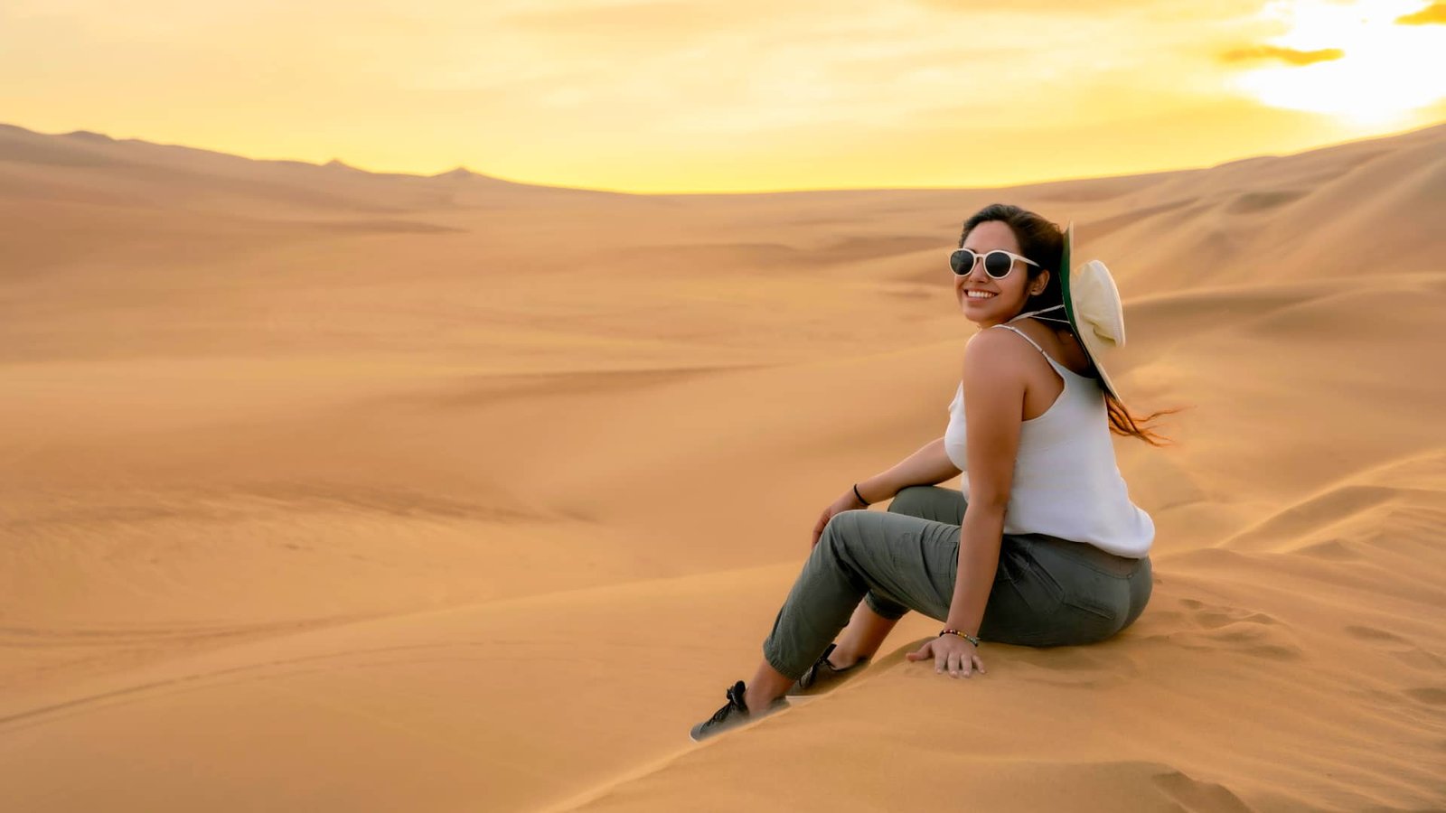 Mujer sentada en la arena contemplando el desierto de Ica.