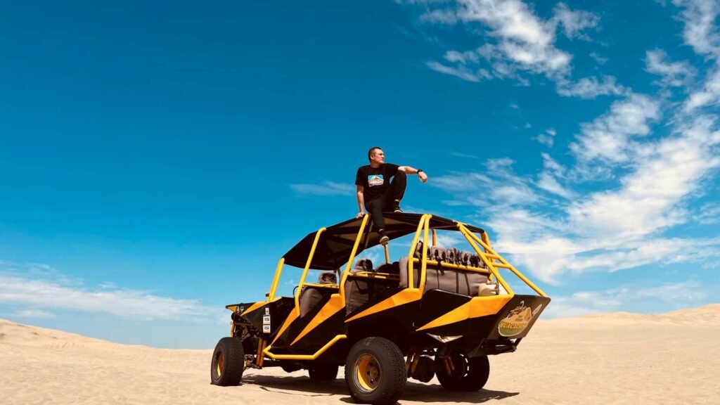 Turista sobre un buggy amarillo en las dunas de Ica bajo un cielo azul.