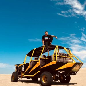Turista sobre un buggy amarillo en las dunas de Ica bajo un cielo azul.